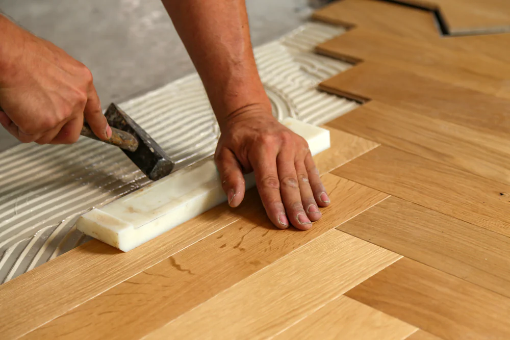 A person using a hammer to lay a wood floor.