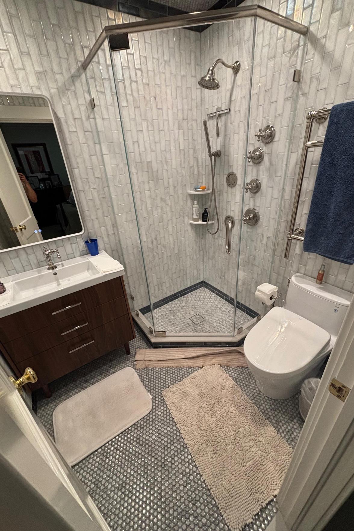 A bathroom featuring a wooden vanity, a white toilet, and a corner glass shower with light tile.